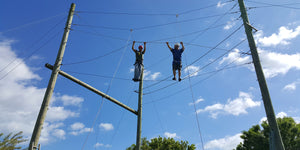Two men in safety gear traverse the wire ropes high above the ground as they go through high ropes course training at a challenge course designed and built by ABEE Inc.