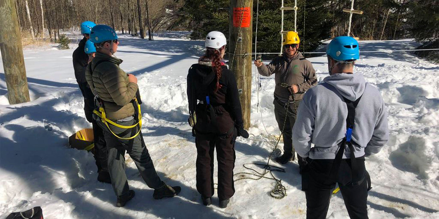 Five adults wear their safety gear and stand in the snow at a their organizations challenge course and zip line being trained and ACCT certified by an ABEE Inc. employee.